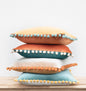 Stack of colorful pillows with pom-pom trim on a light background