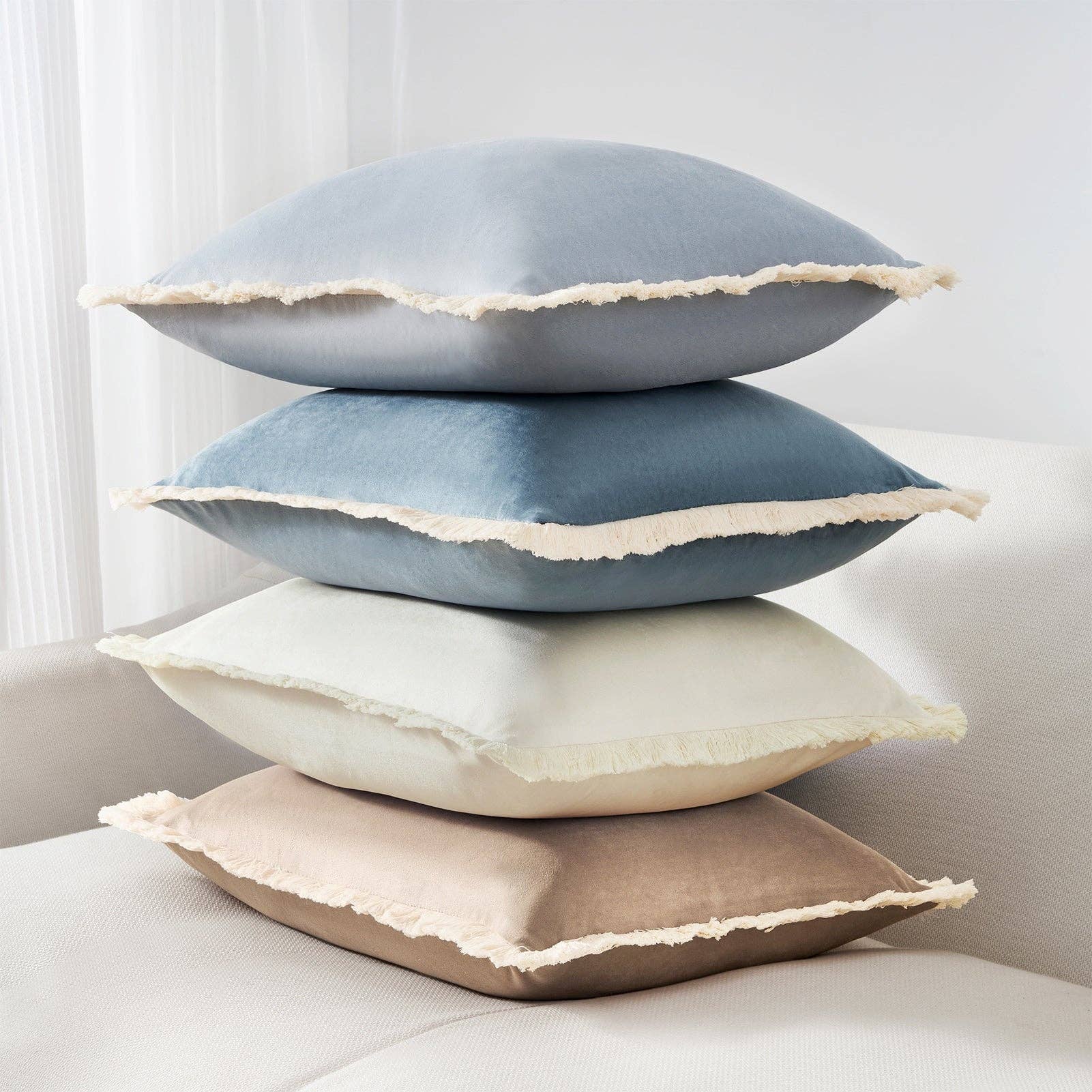 Stack of four decorative pillows in blue, gray, beige, and brown on a light-colored sofa.