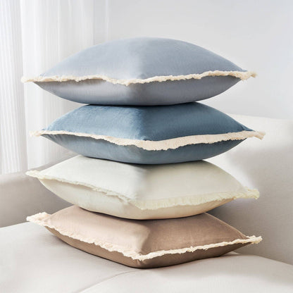 Stack of four decorative pillows in blue, gray, beige, and brown on a light-colored sofa.