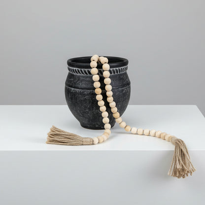Black stone bowl with a white beaded necklace and tassels on a white background