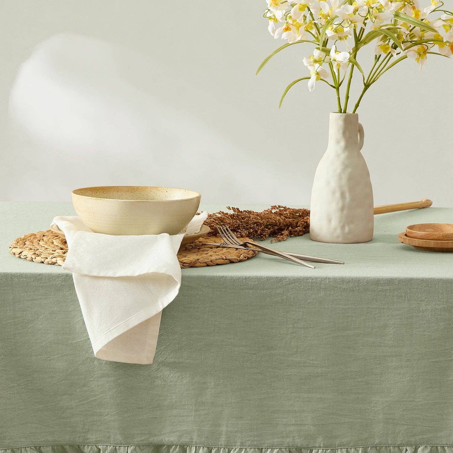 Table setting with a bowl, vase, and cutlery on a green tablecloth.