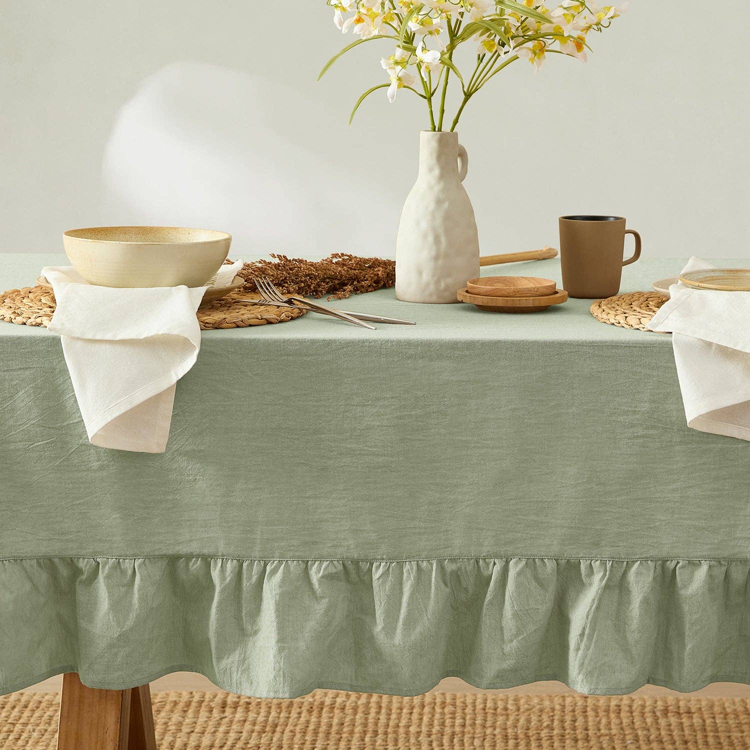 Table setting with a green tablecloth, ceramic vase, and wicker basket on a neutral background