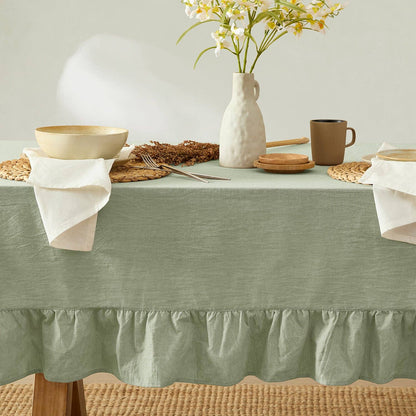 Table setting with a green tablecloth, ceramic vase, and wicker basket on a neutral background