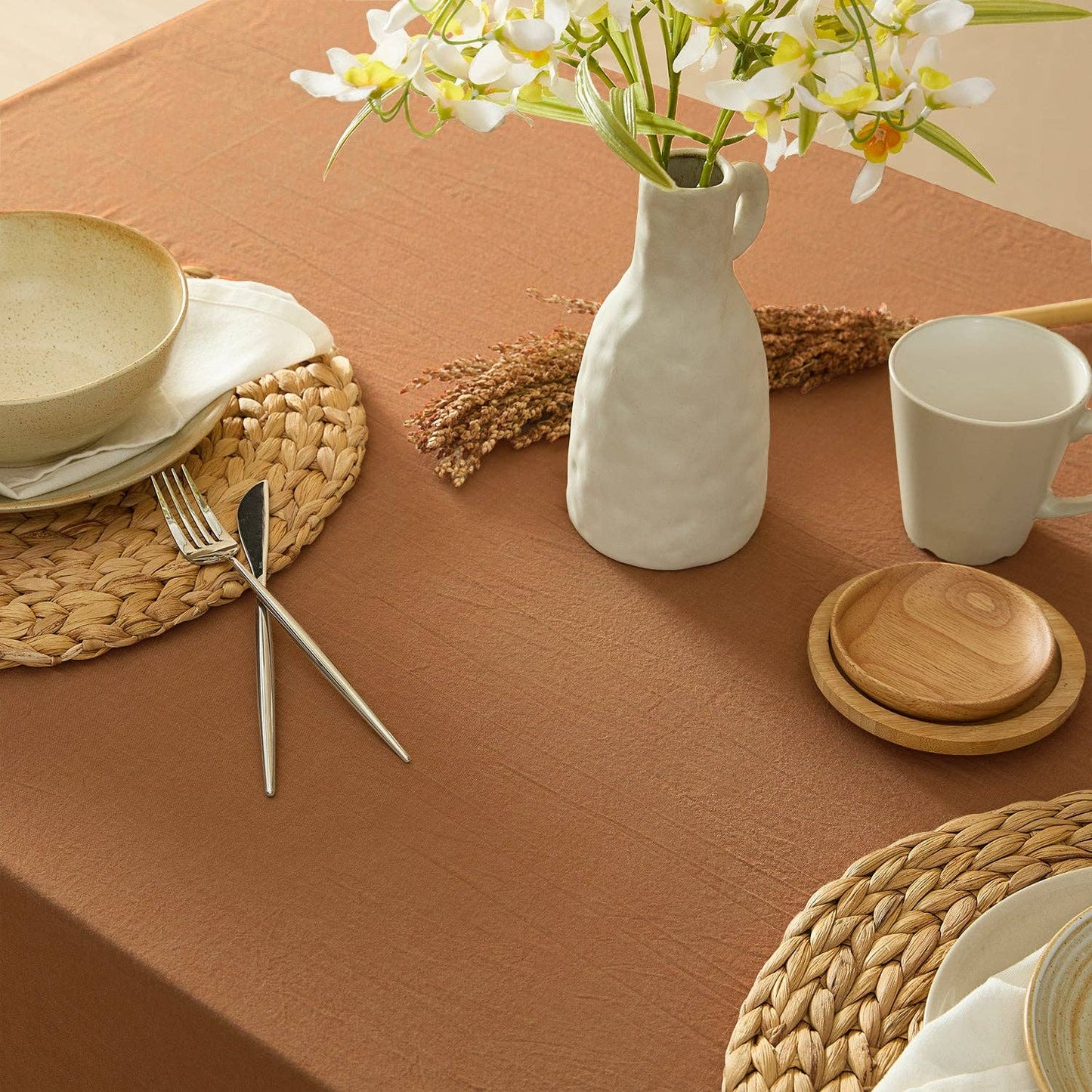 Table setting with a vase of flowers, plates, and cutlery on a brown tablecloth.