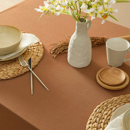 Table setting with a vase of flowers, plates, and cutlery on a brown tablecloth.