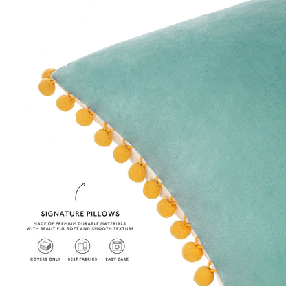 Teal pillow with yellow pom-pom trim on a white background