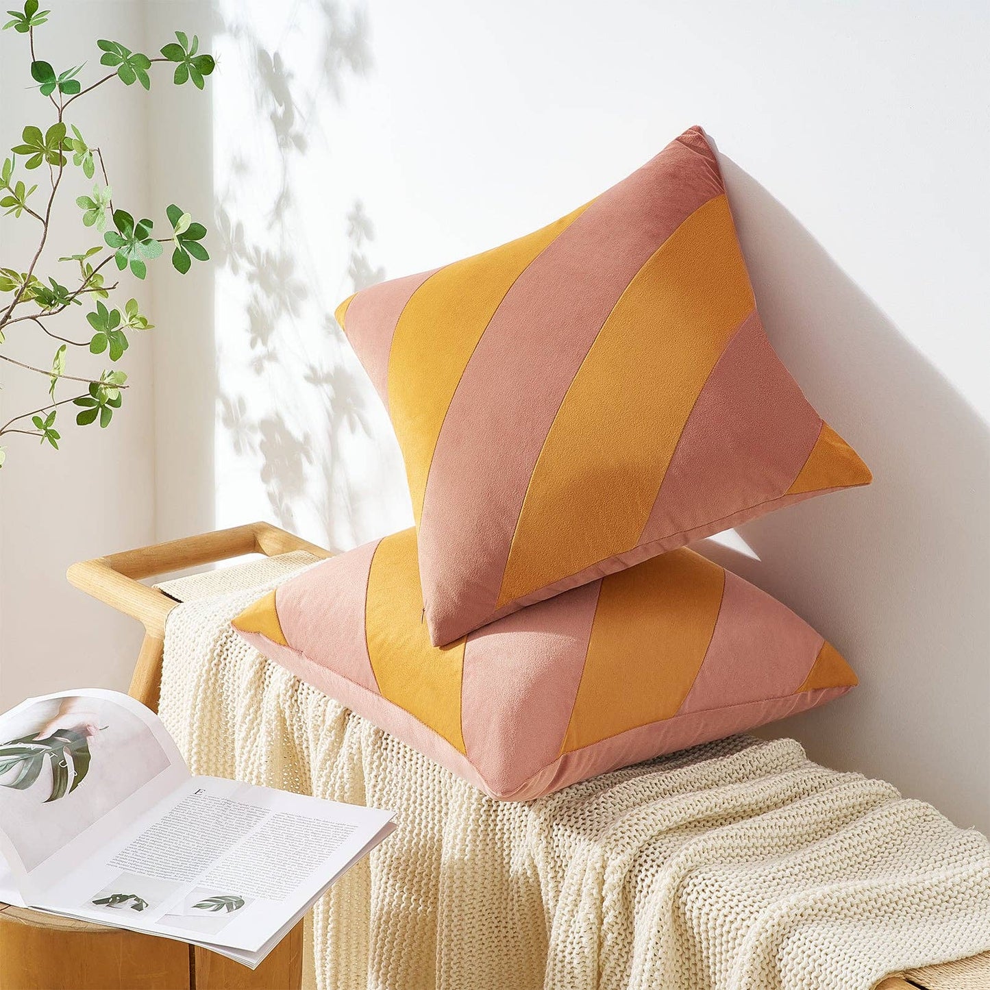 Two colorful pillows stacked on a bench with a plant and magazine in the background