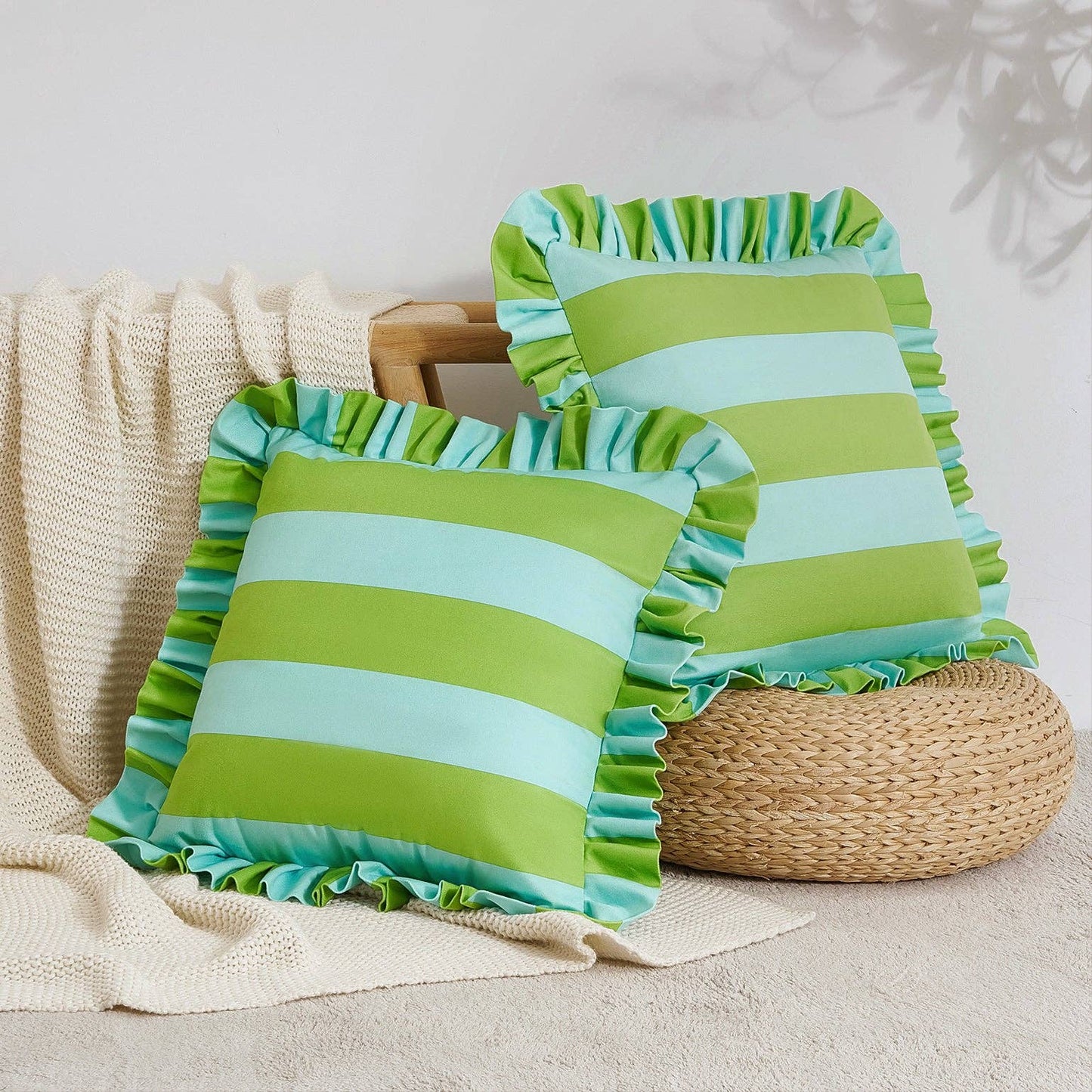 Two green and blue striped pillows with ruffled edges on a neutral background.