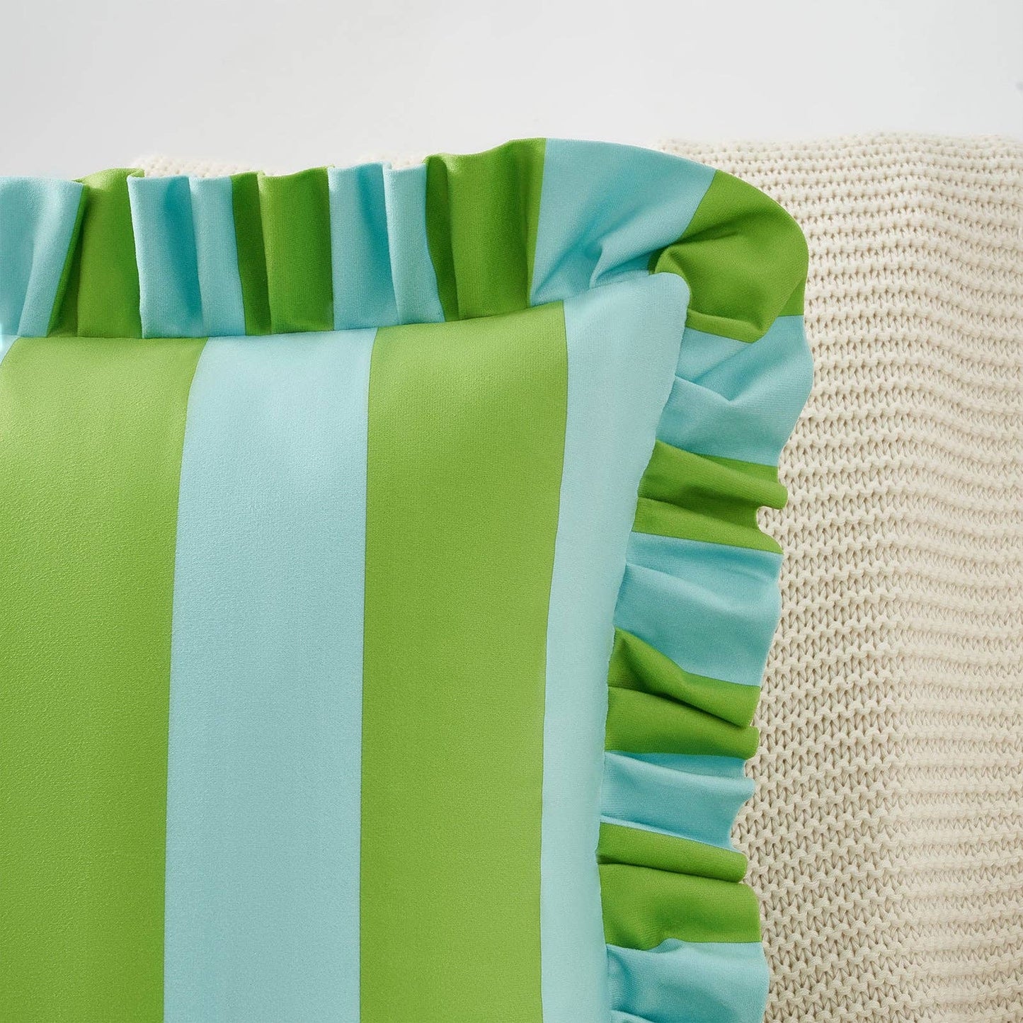 Close-up of a green and blue striped fabric with ruffled edge on a textured beige background.