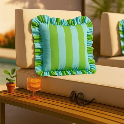 Striped green and blue pillow on a beige outdoor sofa with a small plant and glass of orange juice.