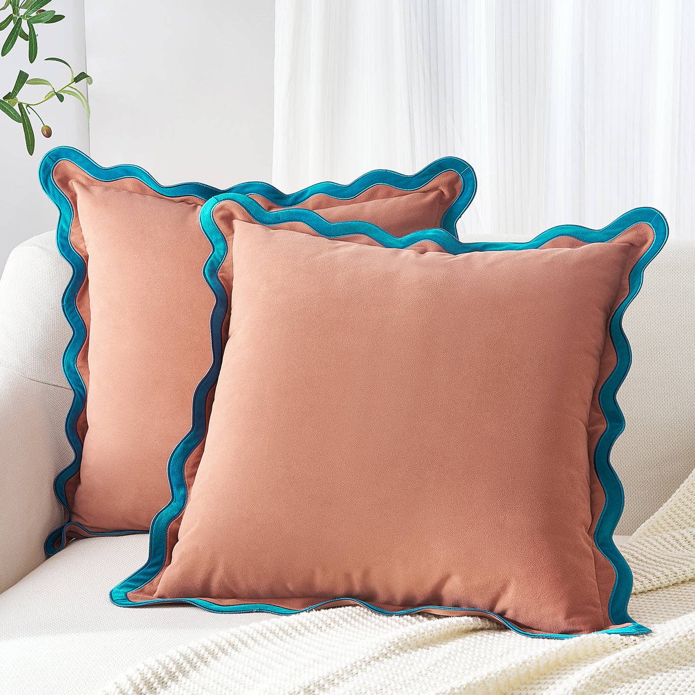 Two pink pillows with blue ruffled edges on a white couch.