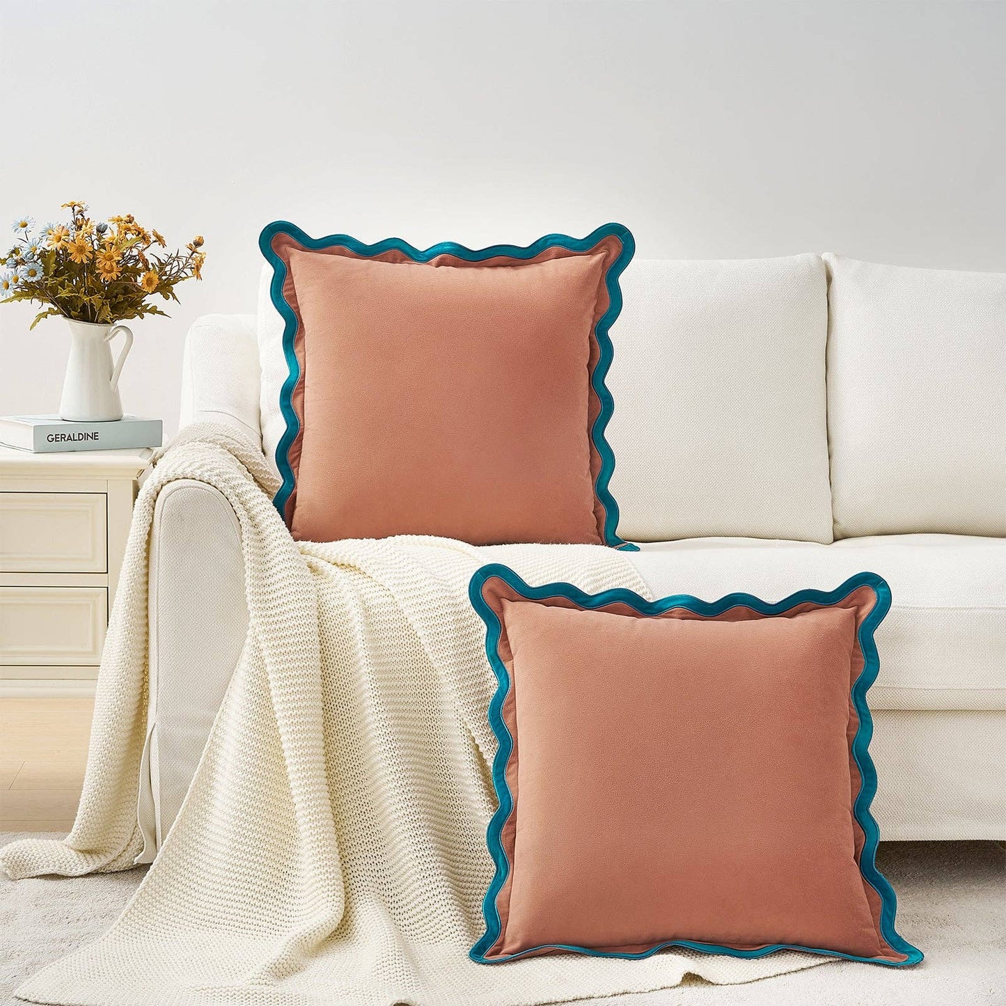 Two pink pillows with blue trim on a white couch in a living room setting.