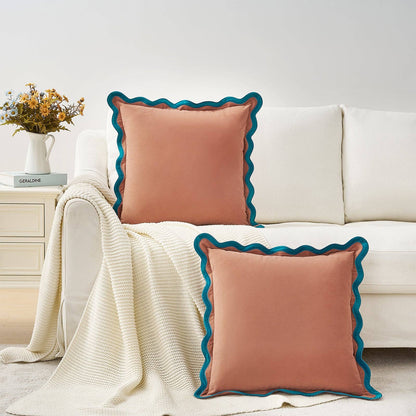 Two pink pillows with blue trim on a white couch in a living room setting.