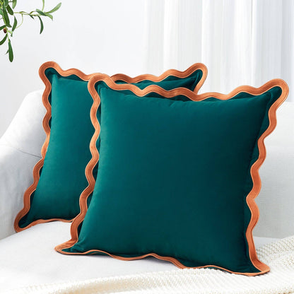 Two teal pillows with brown trim on a white surface.