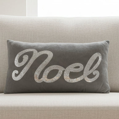 Gray pillow with 'Noel' in silver sequins on a white background