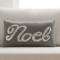 Gray pillow with 'Noel' in silver sequins on a white background