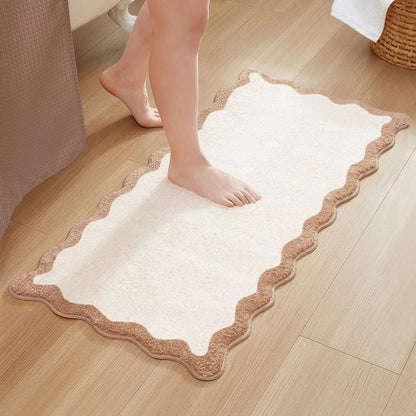 White bath mat with brown border on a wooden floor, person stepping onto it.
