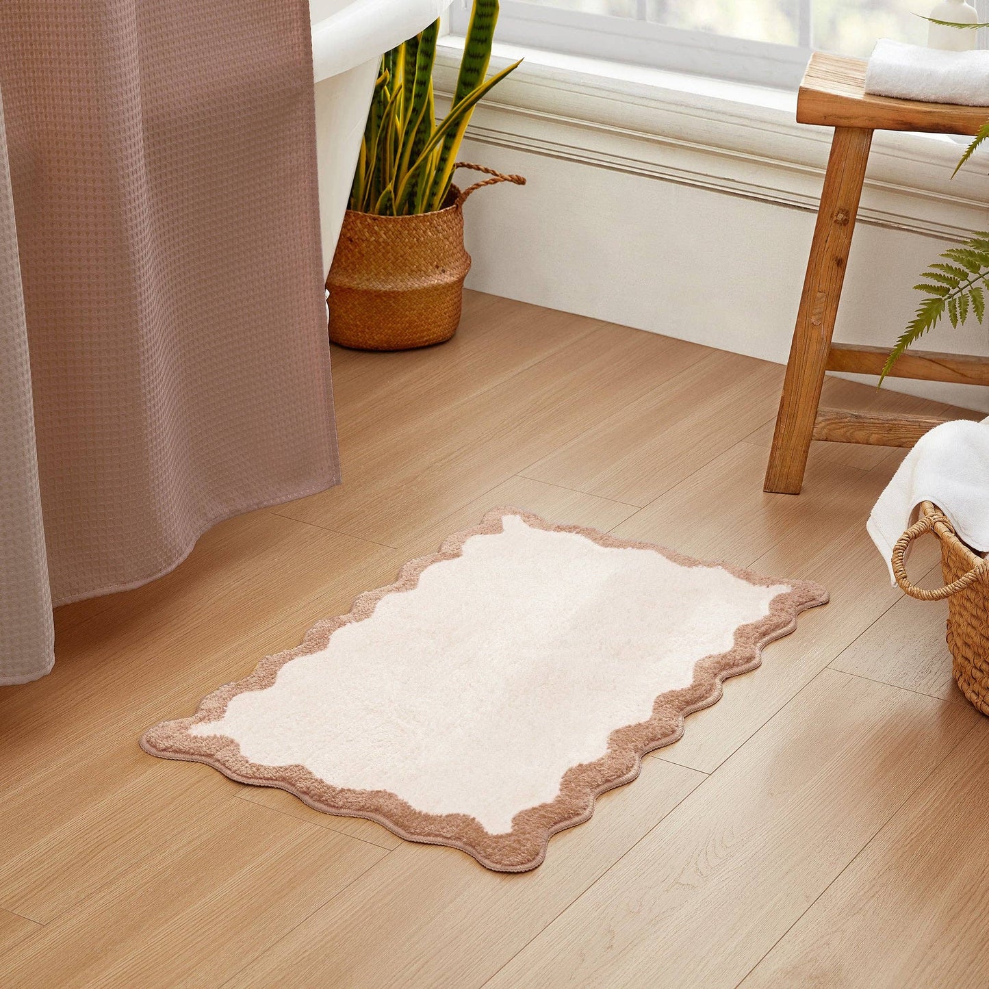 White bath mat with brown border on a wooden floor in a bathroom setting.