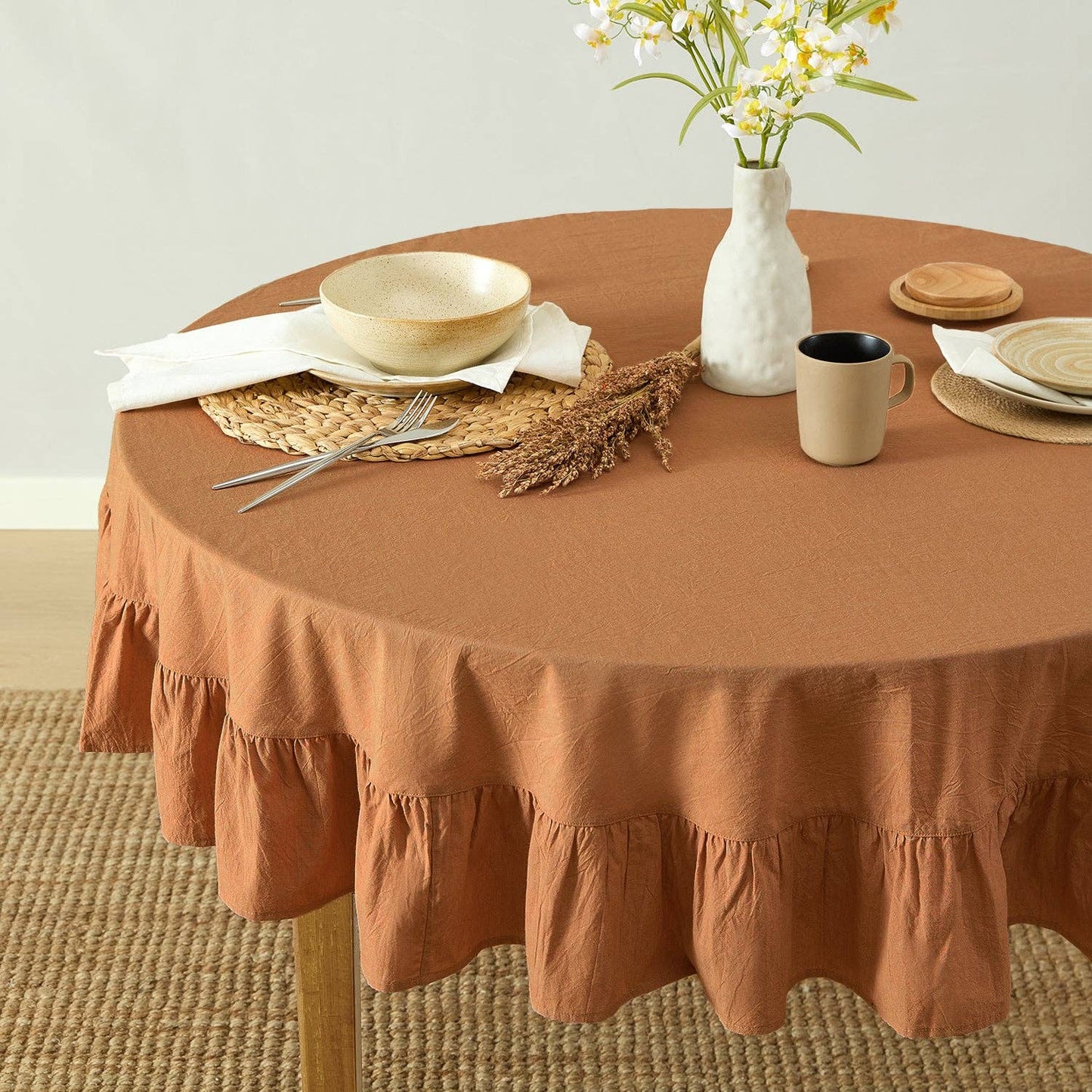 Round table with a brown tablecloth, plates, cups, and a vase with flowers.