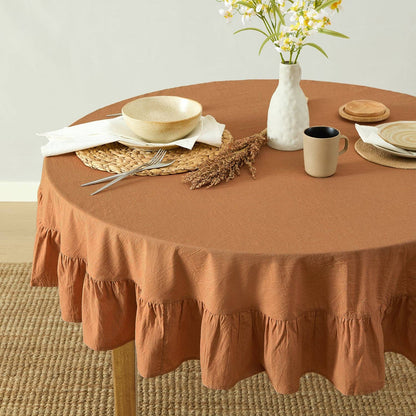 Round table with a brown tablecloth, plates, cups, and a vase with flowers.