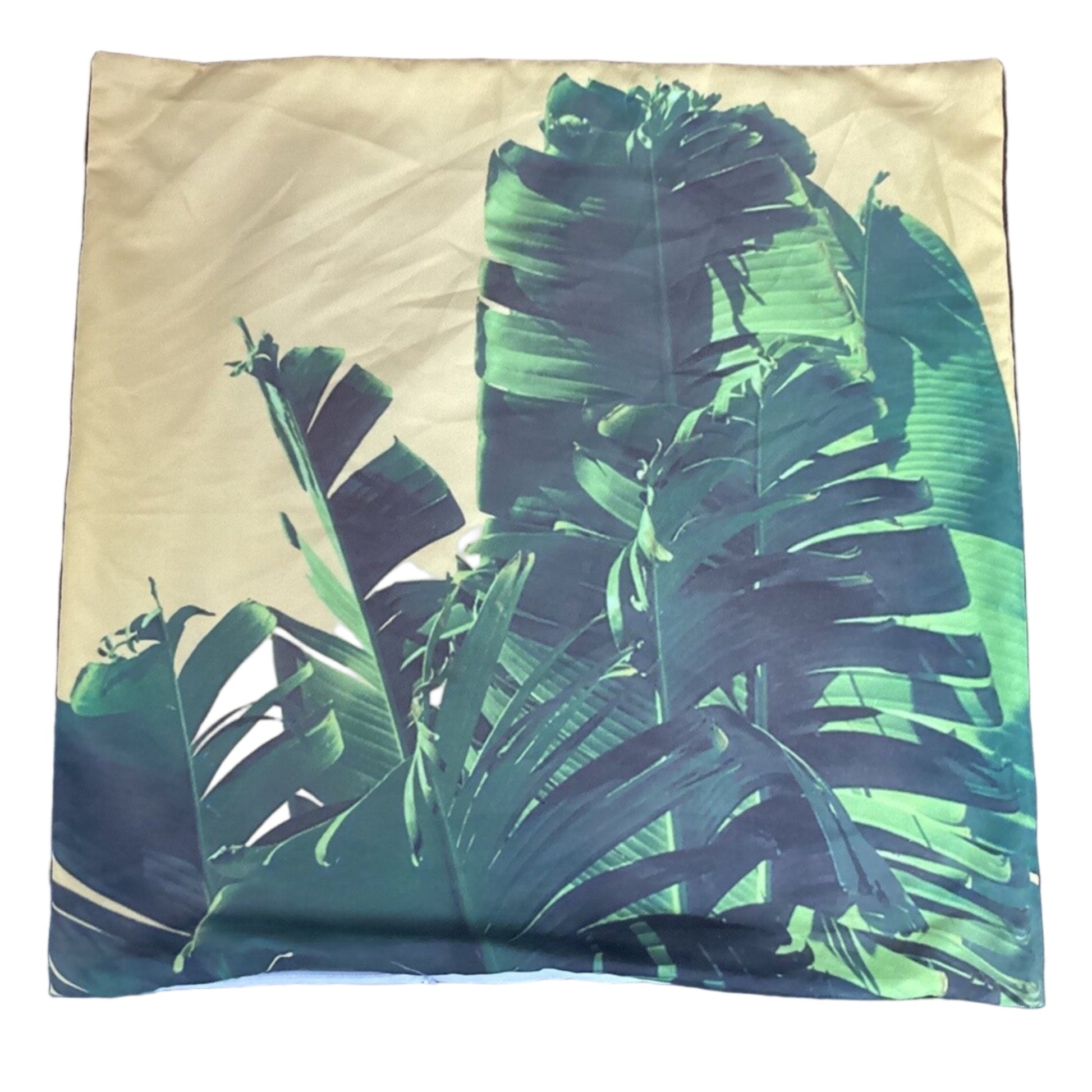 A square pillow featuring a tropical banana leaf print in shades of green and teal on a warm beige background.