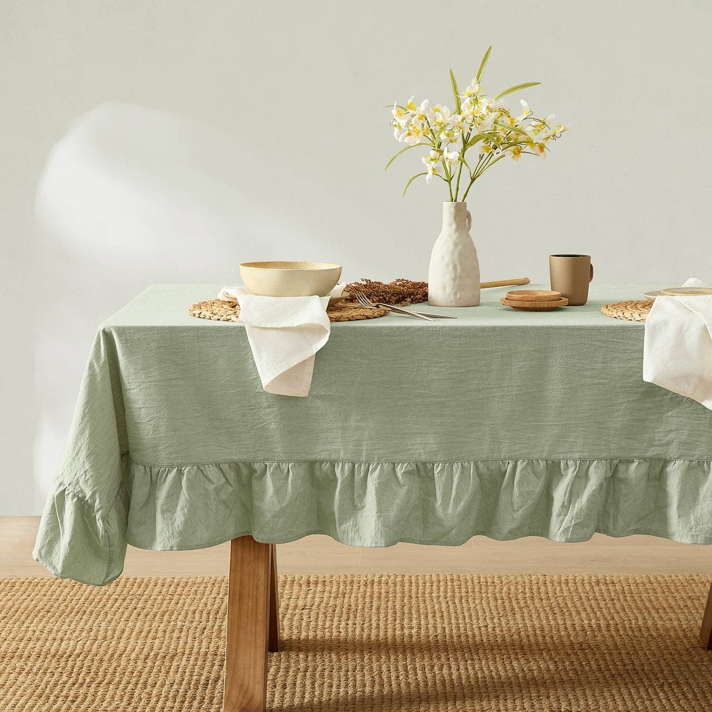 Table set with a green tablecloth, white flowers in a vase, and various items on a neutral background