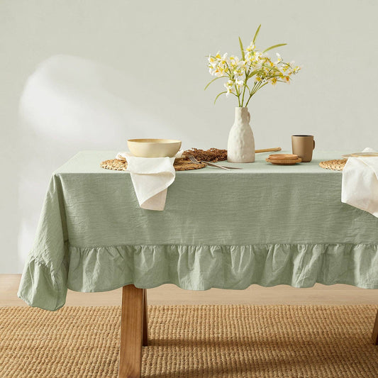 Table set with a green tablecloth, white flowers in a vase, and various items on a neutral background