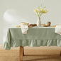Table set with a green tablecloth, white flowers in a vase, and various items on a neutral background