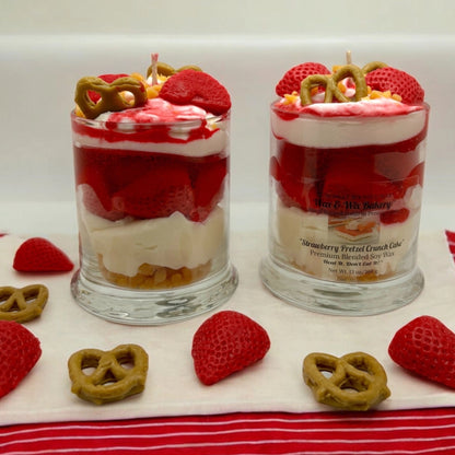 Two glass jars filled with layered strawberry dessert, topped with pretzels and strawberries, displayed on a white cloth with loose strawberries and pretzels around them.