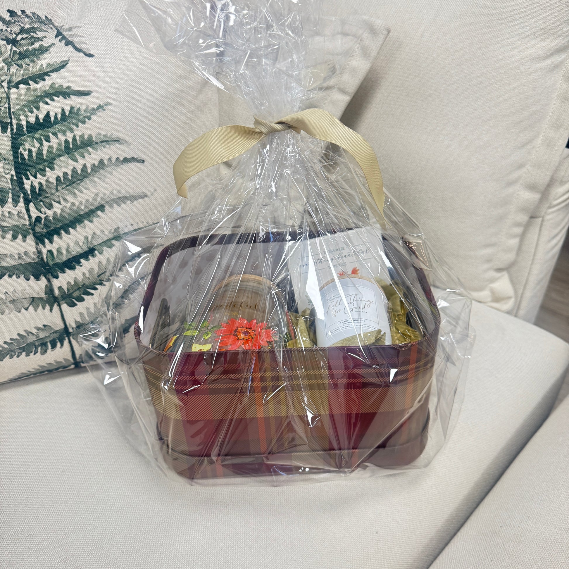 Gift basket wrapped in clear cellophane on a white surface with a plant in the background